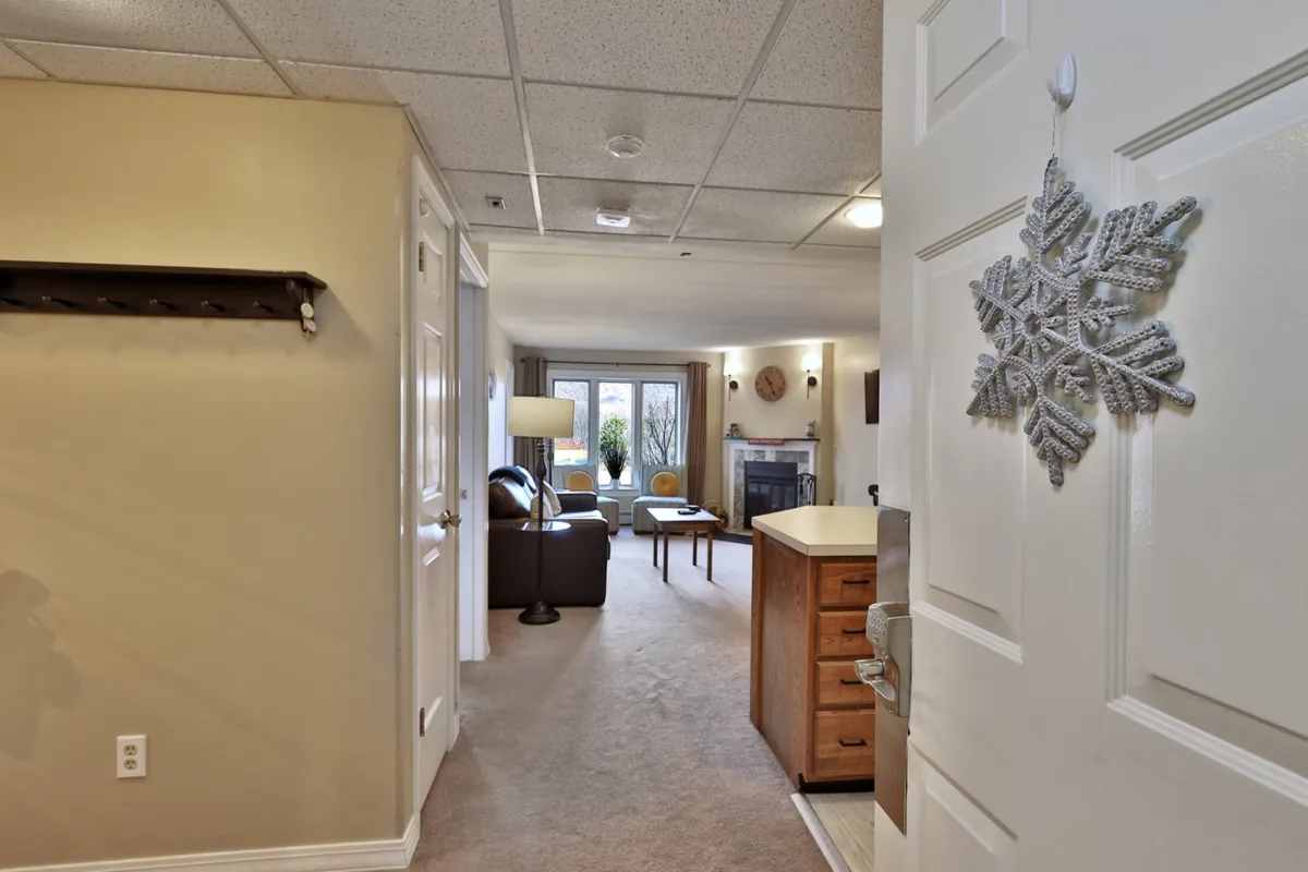 A welcoming entryway opens into a cozy living space, with a kitchen counter visible in the background and a decorative snowflake adding a touch of mountain charm. The layout is bright and open, providing a sense of immediate comfort and connection to the rest of the condo.