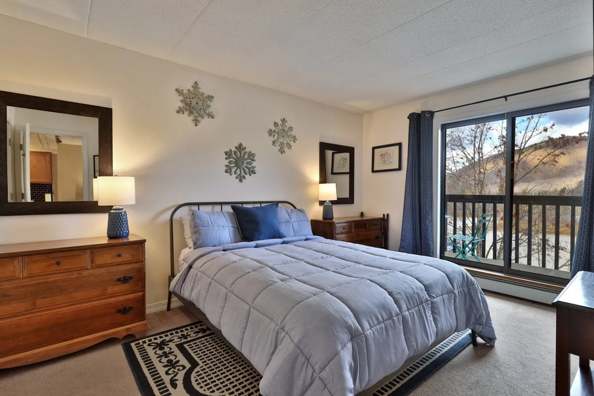A tranquil bedroom scene with a bed, nightstands, and a window view. The setting is cozy and inviting, with natural light softening the room and a reading nook by the window, perfect for quiet reflection.