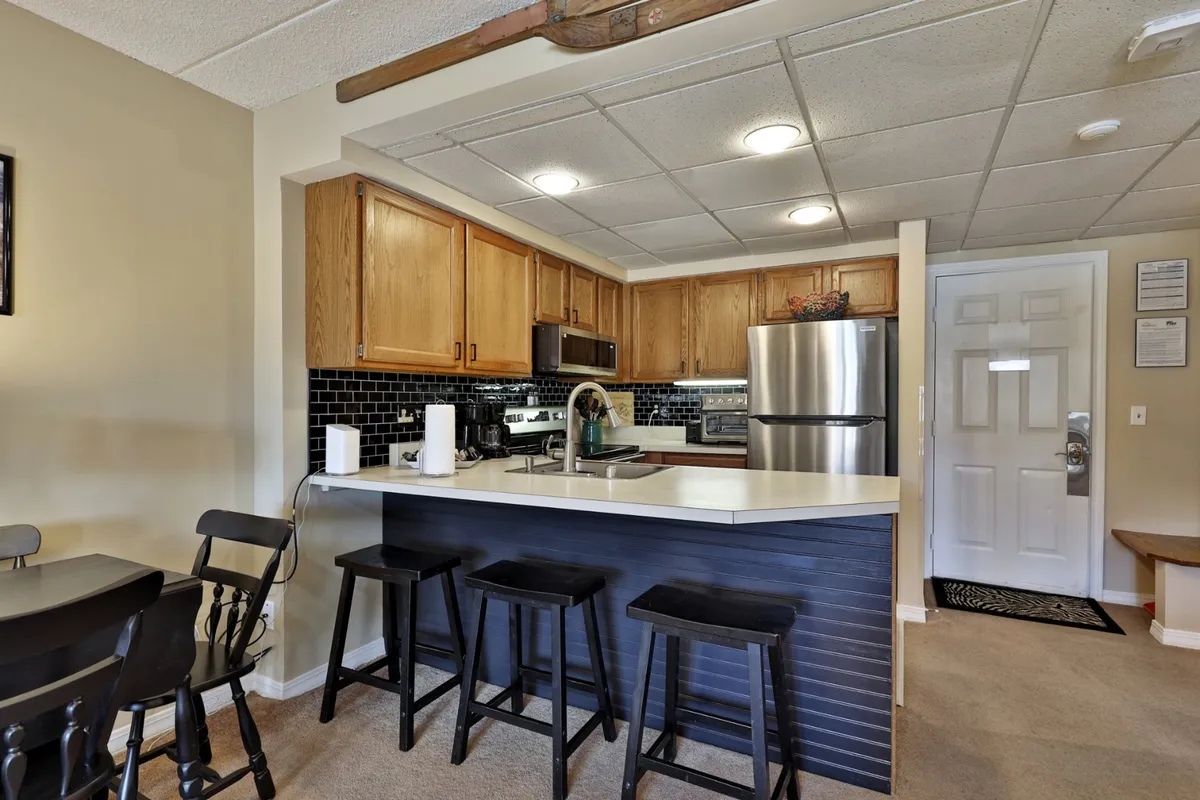 A modern, fully equipped kitchen features a prominent kitchen island with bar stools, stainless steel appliances, and a sleek black backsplash. The setup encourages social cooking and group activities, ideal for preparing après-ski feasts or morning breakfasts.