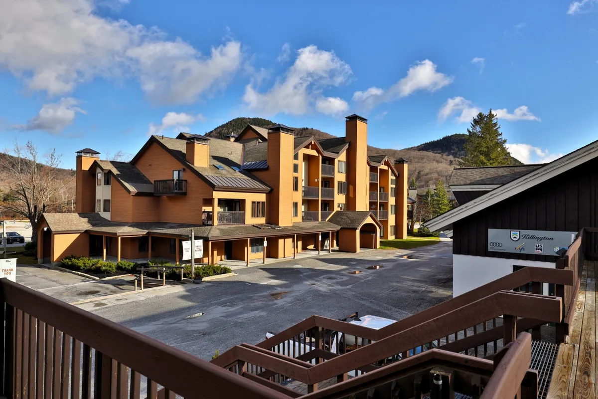 An inviting exterior shot of the multi-story building set against a stunning mountain backdrop. The entrance area and parking are visible, and balconies hint at private outdoor spaces for guests to enjoy the views.