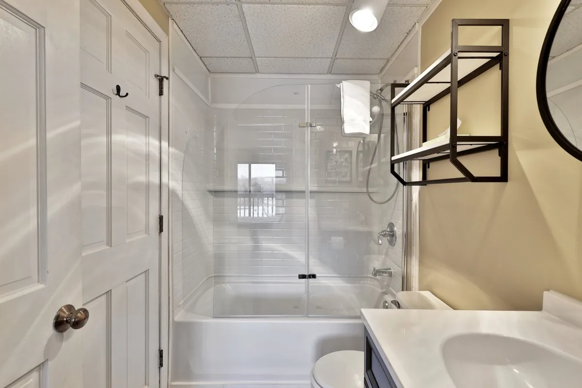 A calm, inviting bathroom featuring a shower area, vanity with mirror, and open shelves. The lighting is soft, and the tidy arrangement of amenities fosters a refreshing and soothing experience, ideal for unwinding after a long day.