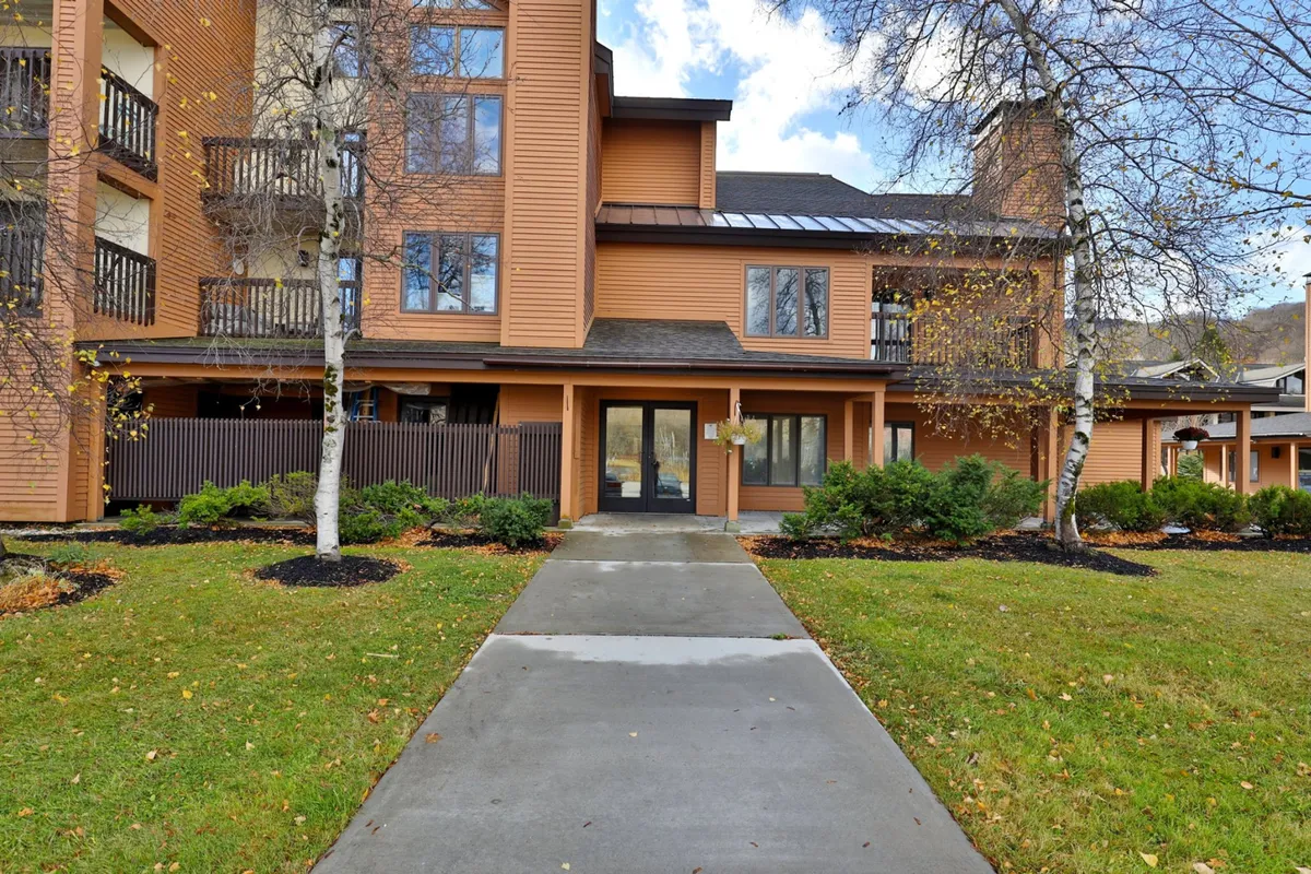 A welcoming exterior perspective featuring the building's entrance pathway, balconies, and lush landscaping. The inviting setting signals opportunities for outdoor relaxation and social gatherings, with balconies perfect for enjoying evening drinks or morning coffee.